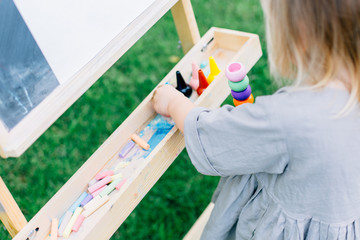 Portrait of adorable baby girl drawing with crayons at easel outdoor .