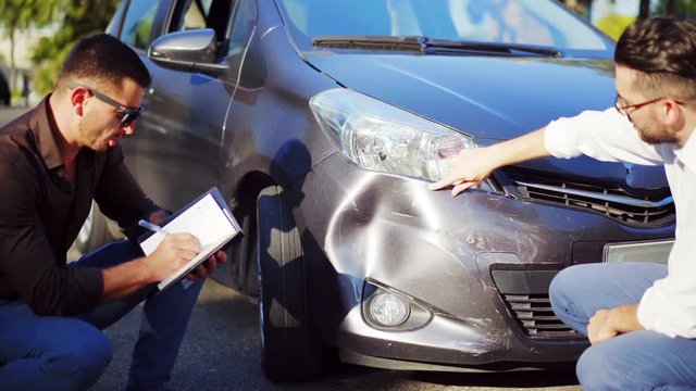 Insurance agent looking at a damaged vehicle and driver after car accident. Road accident. Broken car. Insurance concept. 4K UHD.