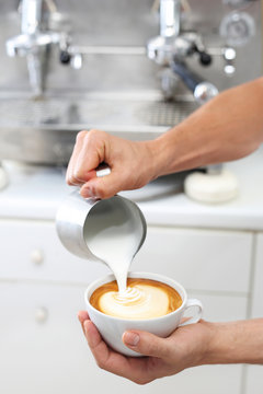 Latte art. 
Barista wykonuje zdobienie na kawie
