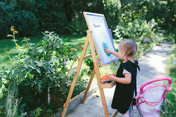 Little cute girl painting on the easel outdoors in the garden