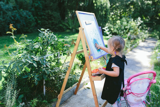 Little cute girl painting on the easel outdoors in the garden