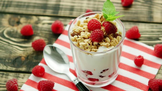 From above shot of glass filled with white yogurt and granola topped with fresh raspberries and served on napkin with spoon