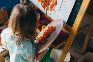 Portrait of adorable little girl drawing with paints and palette at easel