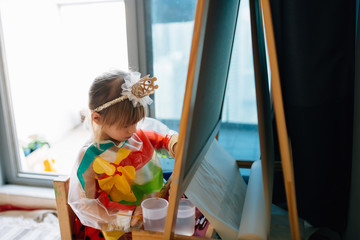 Portrait of adorable little girl drawing with paints and palette at easel