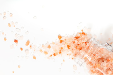 Healthy food concept pink Himalayan salt poured from a glass jar on white background