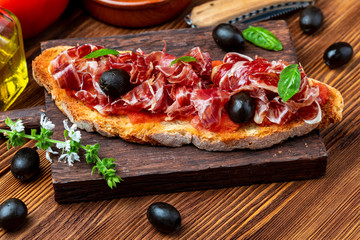 Delicious bread toast with natural tomato, extra virgin olive oil, Iberian ham, black olives and...