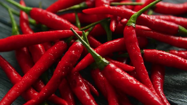 Closeup shot of bright red-colored chili peppers in drops of water lying in heap on wooden table