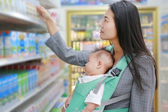 Young business woman choosing breakfast in Convenience Store while carrying her baby boy by hipseat.