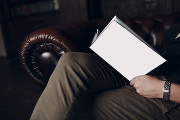 Obraz premium The man is reading book with blank white cover on leather brown chair