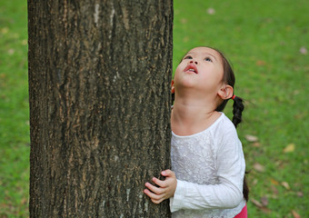 Close-up child girl hugging a tree with looking up at the park.
