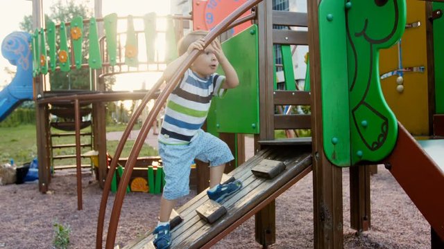 4k video of funny toddler boy climbing on wooden stapladder on children playground at park