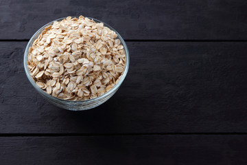 Flakes of oatmeal on wooden boards. Oatmeal on black background. Healthy food for vegans. Preparation of breakfast from natural product. Copy space
