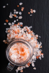 Healthy food concept pink Himalayan salt poured from a glass jar on black slate stone background