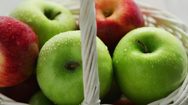 From above shot of white basket full of ripe green and red apples in water drops shining in daylight