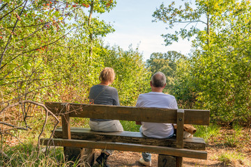 Two unknown elderly people are sitting together on a wooden bench in the forest