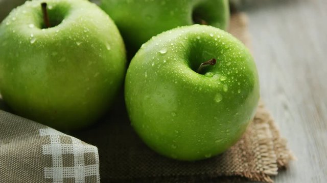 Closeup shot of whole ripe green apples with shiny drops of water composed on canvas napkin in daylight