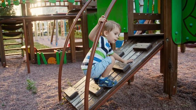 4k footage of little toddler boy struggling to climb on wooden ladder at playground in park