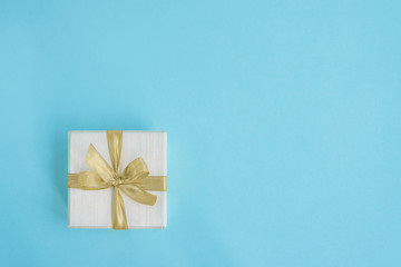 Gift or present box decorated with golden ribbon on light blue background. Top view, copy space.