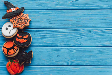 top view of spooky homemade halloween cookies placed in row on blue wooden background