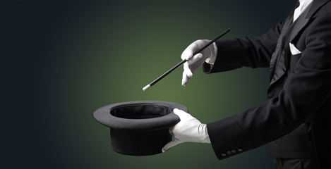 Illusionist white hand wants to conjure with magic wand from a black cylinder something