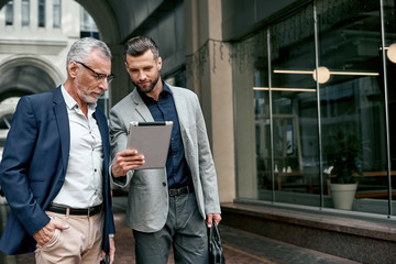 Young and senior business men using digital tablet outdoors on the city background