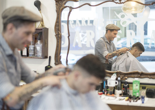 Barbero moderno con vestimenta vintage corta el pelo a joven muchacho veitea&ntilde;ero en barber&iacute;a.