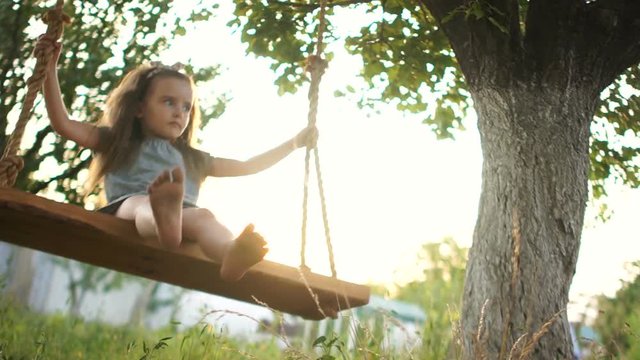 The preschool girl swings on a swing with a serious and focused face. Dynamic video. Happy summer holidays
