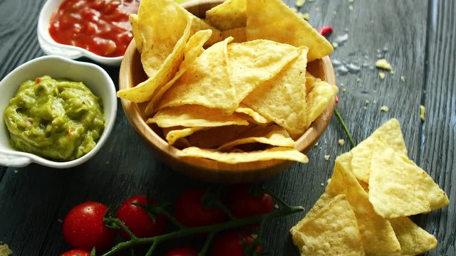 From above view of wooden bowl filled with golden crispy nacho chips on wooden table with lime and chili pepper 