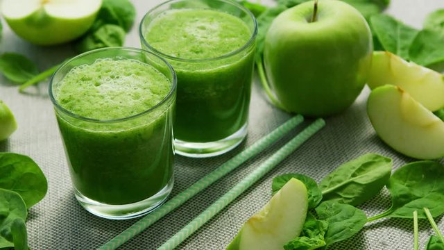 Layout of few glasses filled with green smoothie and served on table with green apples and spinach leaves