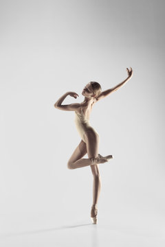 Fototapeta Young graceful female ballet dancer or classic ballerina dancing on white studio. Caucasian model on pointe shoes
