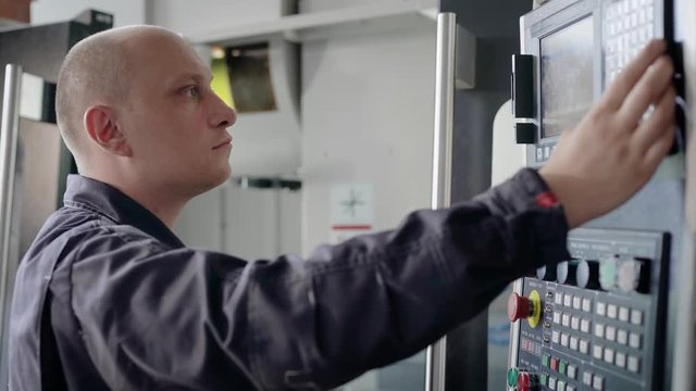 Mechanic programming CNC machine on industrial plant, modern equipment.