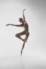 Young graceful female ballet dancer or classic ballerina dancing on white studio. Caucasian model on pointe shoes