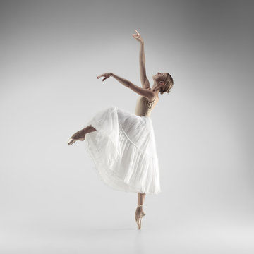 Young graceful female ballet dancer or classic ballerina dancing on white studio. Caucasian model on pointe shoes
