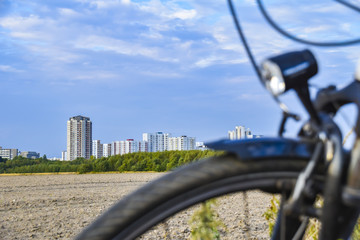 View over the unfocused front wheel of a bicycle across a field to the satellite town of Gropiusstadt in Berlin-Neukölln.