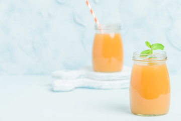 Peach smoothie in glass jars with fresh green mint leaves and straws on blue pastel background.