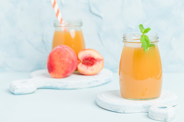 Peach smoothie in glass jars with fresh ripe fruits and green mint leaves on blue pastel background.