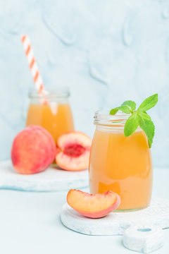 Peach smoothie in glass jars with fresh ripe fruits and green mint leaves on blue pastel background.