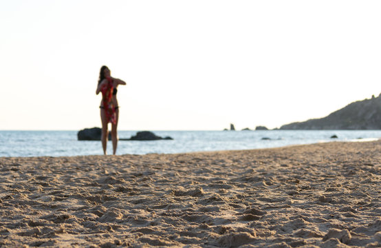 The end of a beautiful day at the beach, sunset light on the sandy surface and a young girl getting ready to leave in the backgroud