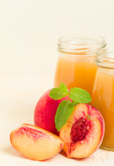 Peach smoothie in glass jars with fresh ripe fruits and green mint leaves on yellow pastel background.