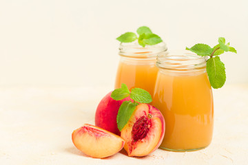 Peach smoothie in glass jars with fresh ripe fruits and green mint leaves on yellow pastel background.