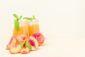 Peach smoothie in glass jars with fresh ripe fruits and green mint leaves on yellow pastel background.