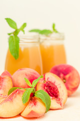 Peach smoothie in glass jars with fresh ripe fruits and green mint leaves on yellow pastel background.