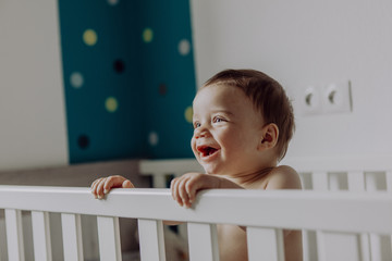 Baby boy standing in his cot, laughing