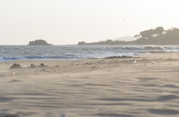 The end of a sunny and windy day at the Falconara beach in Sicily. In this shot is visible the sand moving fast with the strong air and the sun rays seeping into the frame in front of the sea water