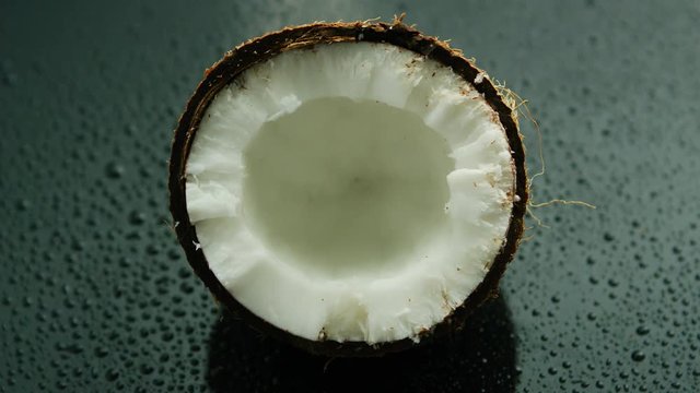 Closeup shot of delicious white coconut half in rough brown shell lying on wet glass surface