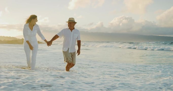 Happy romantic middle age couple enjoying relaxing sunset walk on the beach