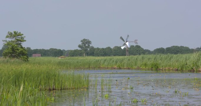 Dutch peat landscape with a long strip of water (petgat) which used to be land from where the peat was harvested. Steel drainage windmill rotates. WIEDEN-WEERRIBBEN NATIONAL PARK