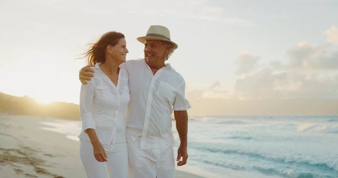 Happy romantic middle age couple enjoying relaxing sunset walk on the beach