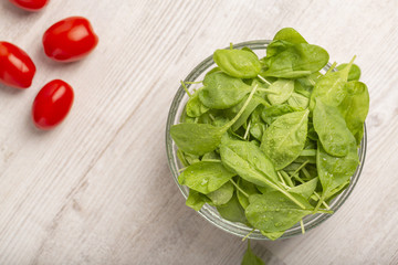 Fresh spinach leaves and tomatoes on light background