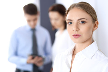 Beautiful blonde businesswoman standing straight in a brightly lit office at the background of colleagues or partners. Business concept